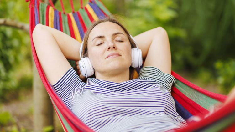 Bildet viser en kvinne som ligger i en hengekøye med headset. 